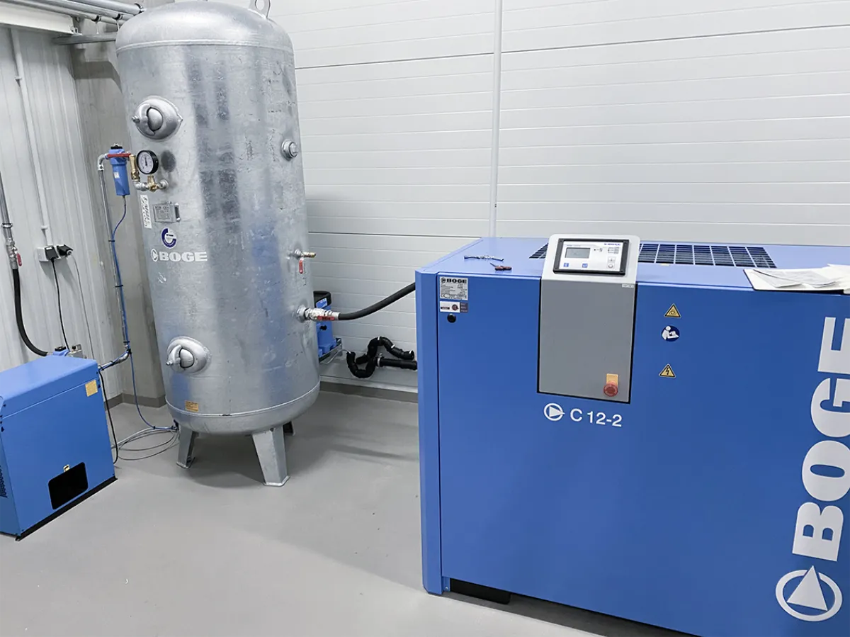 Moderne Druckluftanlage mit Kompressor und Druckluftspeicher zur Versorgung einer Nutzfahrzeugwerkstatt. Die technische Infrastruktur ermöglicht den zuverlässigen Betrieb pneumatischer Werkzeuge und Versorgungssysteme in der Werkstattgrube.