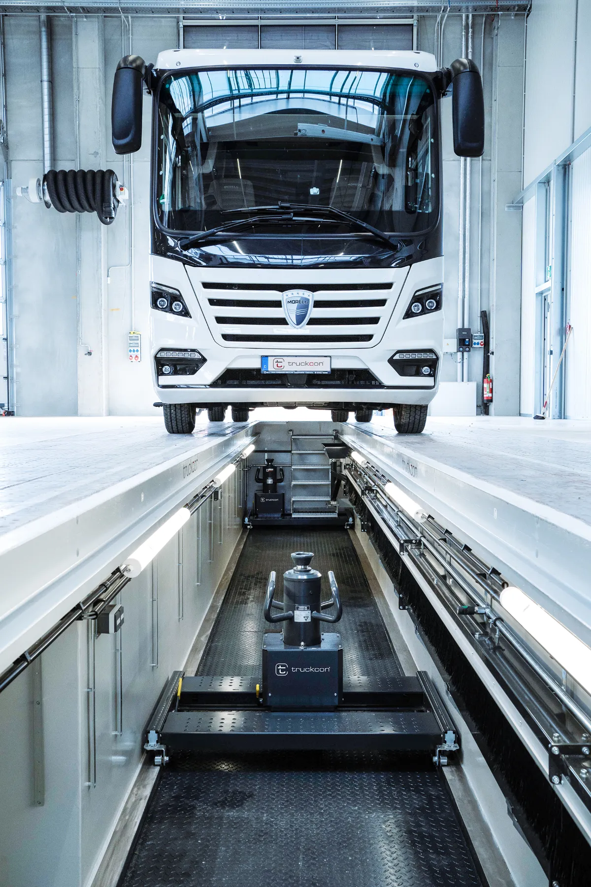 Frontansicht eines Reisemobils über einer modernen truckcon Werkstattgrube in einer hellen Servicehalle. Die Aufnahme zeigt eine professionell ausgestattete Wartungsgrube mit integrierter Beleuchtung, Versorgungstechnik und Hebesystemen für effiziente Arbeiten an großen Nutzfahrzeugen und Wohnmobilen.