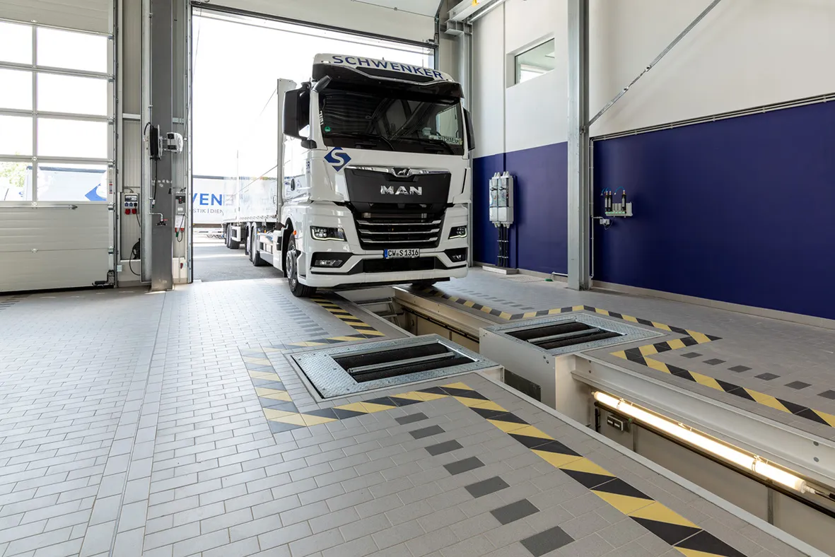 Nutzfahrzeug auf einem Rollenbremsprüfstand in einer modernen Servicehalle. Die Aufnahme zeigt die Kombination aus Werkstattgrube, Prüfstandtechnik und Sicherheitsmarkierungen für präzise Bremsenprüfungen an LKWs und Transportfahrzeugen.